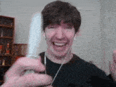 a man wearing headphones is laughing while holding a remote control in his hand .