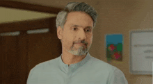 a man with gray hair and a beard is standing in front of a door and smiling .