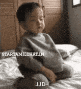 a baby is sitting on a bed with its eyes closed .
