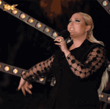 a woman in a black dress singing into a microphone with an x on the bottom left