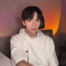 a young man in a white hoodie is sitting in a chair looking at the camera .