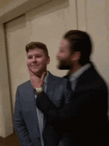 two men in suits are standing next to each other and one is touching the other 's neck .