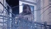 a woman with blood on her face is standing on a balcony looking out of a window .