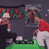 a couple of men standing next to each other in front of a christmas sign .