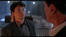 a man in a suit and glasses talks to another man in a dark room