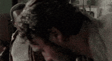 a man in a plaid shirt is talking to another man in front of a row of guns .