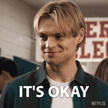 a man is smiling in front of a sign that says it 's okay on it