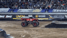 a monster truck is driving on a dirt track with a utah sports commission banner in the background