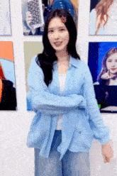 a woman in a blue shirt and jeans is standing in front of a wall with pictures of herself on it .