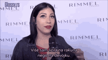 a woman is talking into a microphone in front of a wall with rimmel london written on it