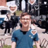 a young man wearing glasses and a blue shirt is standing on a street with hearts around him .