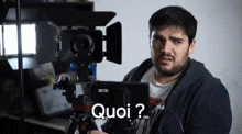 a man with a beard is holding a camera and says quoi
