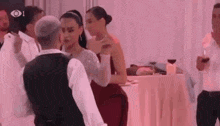 a man and a woman are dancing at a wedding reception while a man holds a glass of wine .