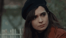 a woman wearing a black beret and a red coat is standing in front of a white fence .