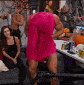 a man in a pink dress is standing in front of a table with cans of dr pepper
