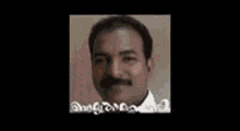 a man with glasses and a mustache is standing in front of a wall .