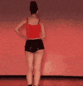 a woman in a red tank top and black shorts is dancing in front of a red wall