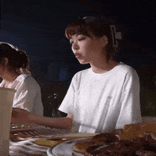 a woman in a white shirt is sitting at a table with a plate of food in front of her .