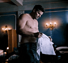 a shirtless man is standing in a dark room holding a white towel