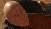 a bald man in a brown shirt is laying on the ground