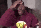 a man in a red hoodie is sitting on a couch holding his head .