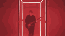 a man is playing a guitar in a red room with neon lights .