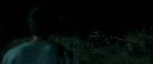 a man is standing in a field of tall grass at night looking at a car .