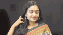 a woman is wearing a saree and earrings and is looking down at her hair .