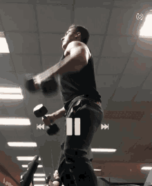 a man is lifting a dumbbell in a gym with a pause button on the bottom right