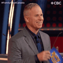 a man in a suit and tie is smiling while holding a piece of paper that says ' family feud canada ' on it