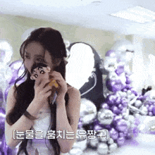 a woman is standing in front of a bunch of balloons holding a stuffed animal .