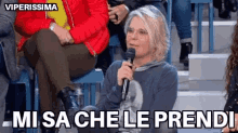 a woman is sitting in a crowd holding a microphone and says mi sa che le prendi