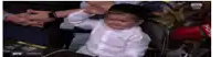 a little boy in a white shirt is sitting in a chair with his hands on his head .