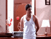 a man in a white tank top is standing in a room