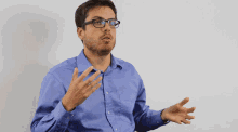 a man wearing glasses and a blue shirt talks with his hands outstretched