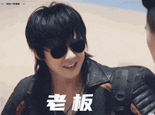 a man wearing sunglasses and a leather jacket with chinese writing on the bottom