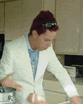 a man with red hair wearing sunglasses and a white jacket is cooking in a kitchen