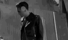 a black and white photo of a man in a leather jacket standing in front of a mirror .