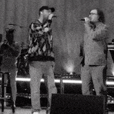 a black and white photo of two men singing into microphones on a stage