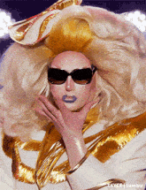 a drag queen wearing sunglasses and a white and gold outfit has the word tumblr on the bottom