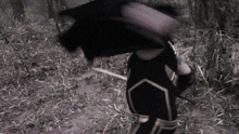 a person in a black and gold outfit is holding a sword in the woods