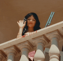 a woman waves from a balcony with a gun behind her