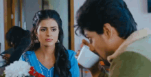 a man is drinking from a cup while a woman looks at him .