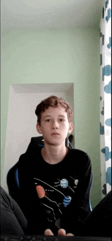 a young boy wearing a black shirt with planets on it sits in a chair