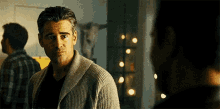 a man in a sweater is looking at another man in a dark room .