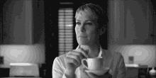 a black and white photo of a woman holding a cup of coffee .
