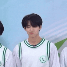 a young man wearing a white and green basketball jersey with the letter l on it is standing next to another young man .