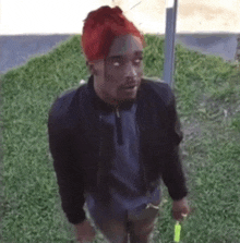 a man with red hair and a beard is standing in the grass holding a green stick .