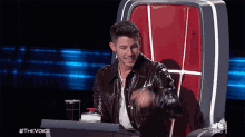 a man in a leather jacket is sitting in a chair with a nbc logo on it