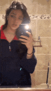 a woman is taking a selfie in a bathroom mirror with her phone .